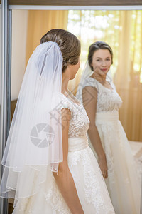 服装袍穿着婚纱的美丽年轻新娘照着镜子女图片