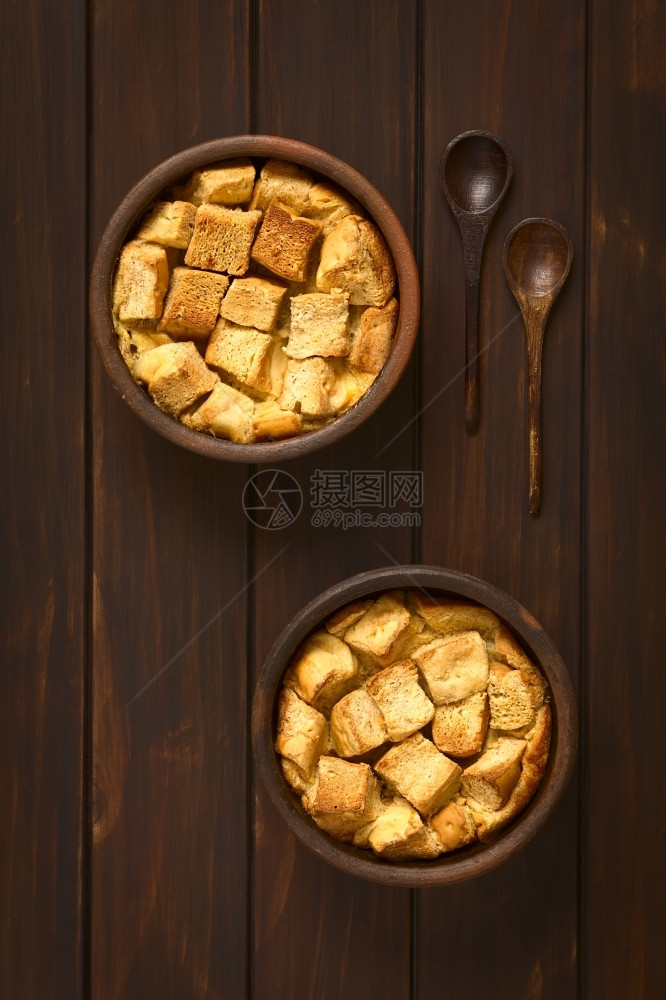 垂直的甜两碗由面包布丁制成的硬饼牛奶鸡蛋肉桂糖和黄油制成的粗面包布丁用天然光照在黑木头上制作图片