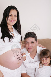 期待与怀孕母亲一起在沙发上放松的一家庭加上爱你在她肚子上西班牙裔孩子图片