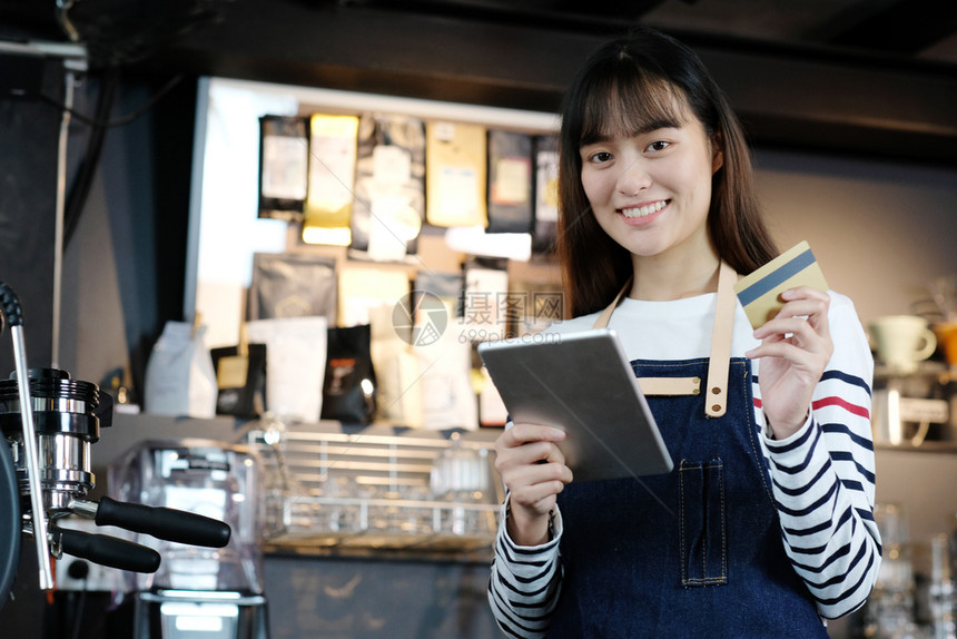 女士职业员使用平板牌和在咖啡柜台持有信用卡食品和饮料商业概念的年轻女亚洲律师协会图片