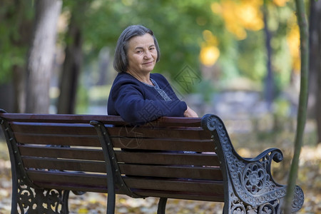 年龄幸福农村秋天公园坐在长椅上的年老妇女看着镜头并微笑图片