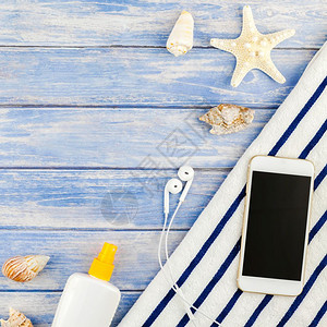 空白的防晒霜海滩毛巾智能手机海贝壳象鱼的顶端视图其背景为面糊蓝木板底并附有空间模拟文本版板SpreplaceModupBlook背景图片