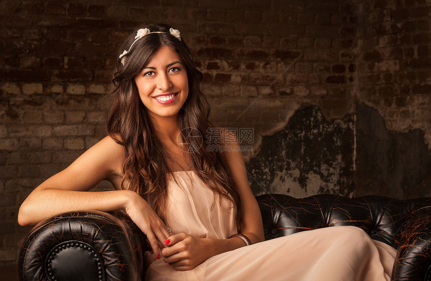 一个漂亮的黑发女孩坐在有砖墙背景的皮沙发上书年轻的棕色图片