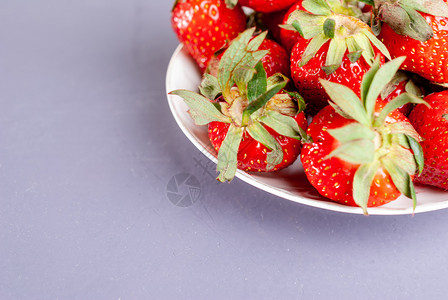 白色盘子紫背景的新鲜草莓紫色背景的红草莓和鲜食物叶子多于图片