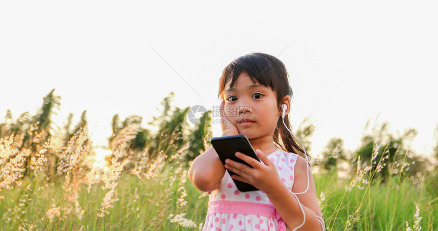 亚洲女童听手机的音乐和歌唱夏天在草地上欢乐自然而头发聆听亚洲人图片