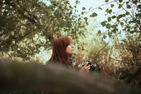 请享用老的照片年轻女子用旧的模拟相机在森林里拍照图片