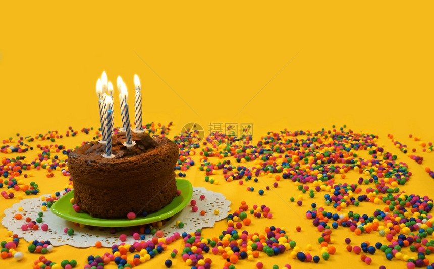 包围经过巧克力生日蛋糕7个蓝色和白蜡烛在小绿色盘子上点亮周围是黄色背景的糖果球有复制空间的图像快乐图片