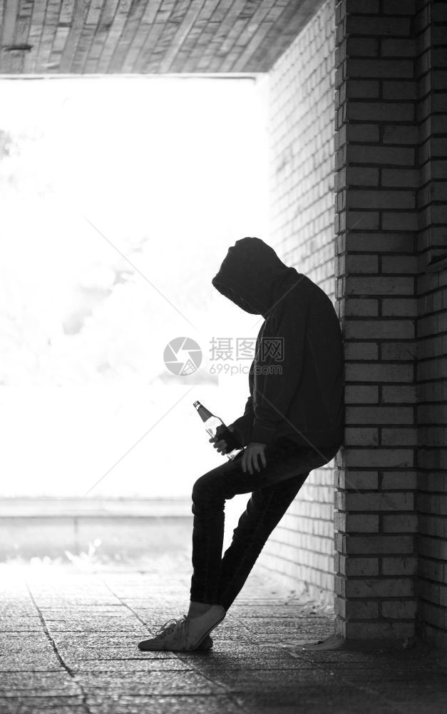 坏的孤单青少年休修会站在黑暗的门道上啤酒瓶装着汗衫和兜帽消极的保持图片