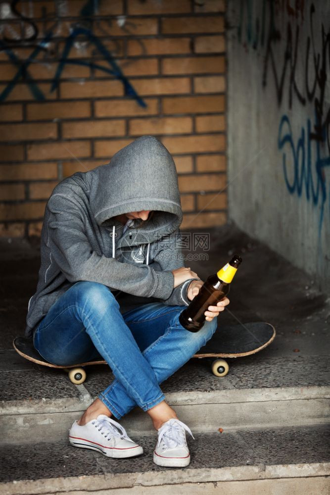 孤独的少女坐在黑暗门道上拿着啤酒瓶装汗衫和兜帽坏的瓶子无家可归图片