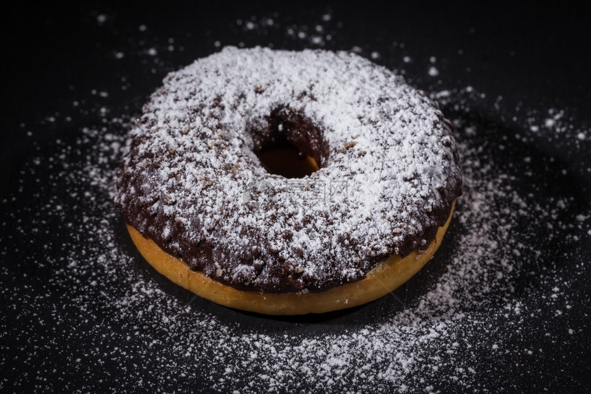 糖粉洒在美味甜圈上加巧克力棕色的黑粉末图片
