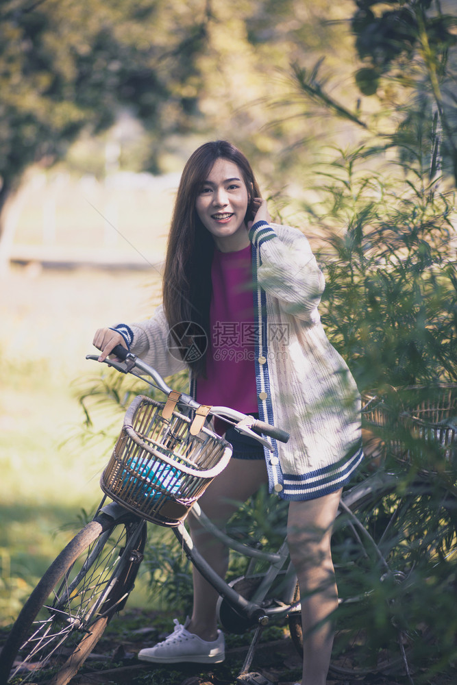在绿色公园骑着旧自行车的年轻女士们喜悦地在绿色公园中亚洲人吸引的闲暇图片