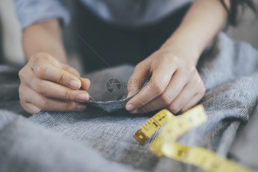 衣服工作室在桌上缝纫的年轻女裁穿着工作桌上的锯皮夹克针线活图片