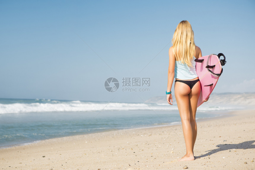 冲浪女孩带着板在海滩上散步背影图片