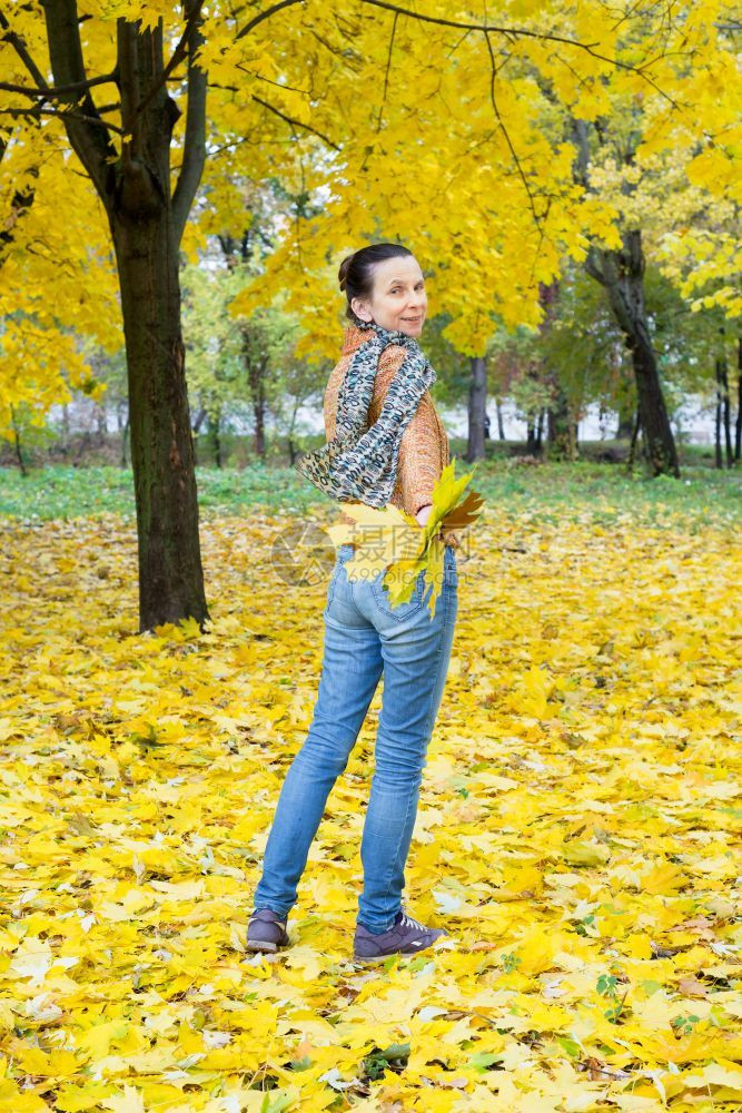 橙跑步白种人一个笑着的成年caucasians女人秋天在公园里带着黄色的树叶逃跑图片
