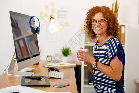 在办公室工作并喝咖啡的中年妇女技术愉快陈年图片