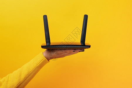 调制解器黄色背景上女手的黑色wifi路由器转变连接的图片
