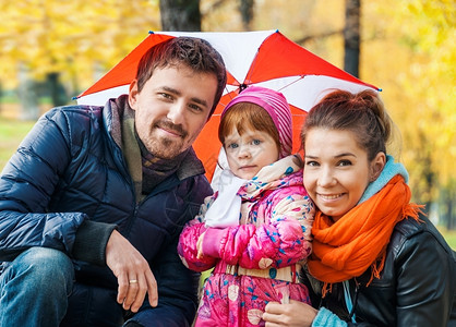 女士男人秋天公园的雨伞下快乐年轻家庭图片