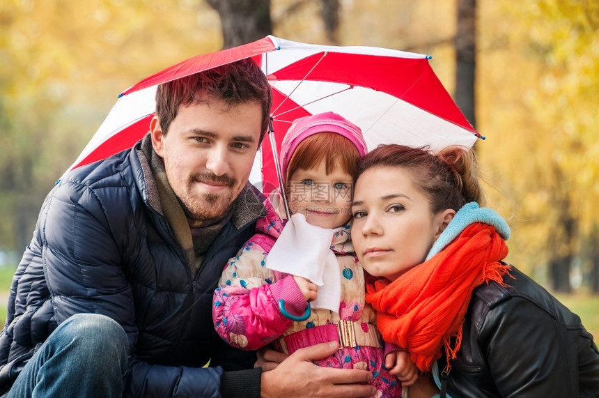 孩子手秋天公园的雨伞下快乐年轻家庭草图片