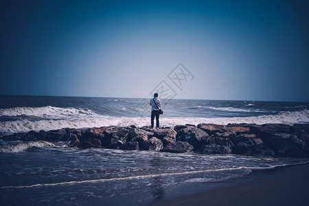 人站在海滩和边的岩石风景上海洋远足旅游图片