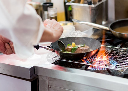 美味的厨师在房炉灶的煎锅中用火焰做饭制造烹饪图片
