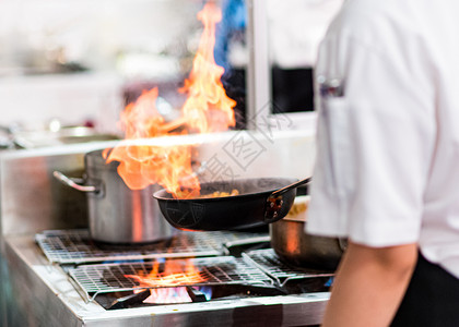 专业的厨师在房炉灶的煎锅中用火焰做饭午餐一顿图片