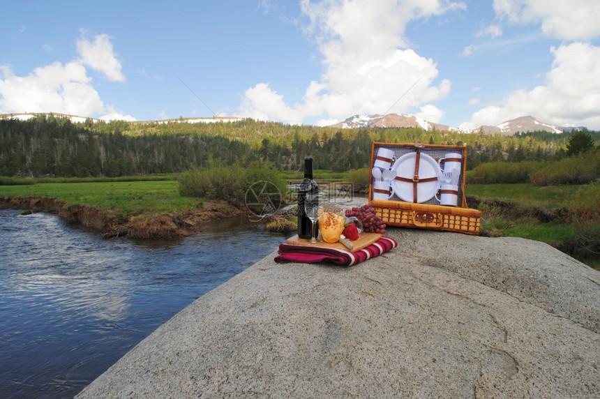 水果和葡萄酒在风景优美的山上野餐底有一片草地和河流位于边的PicnicOnTheRiver健康明亮的图片