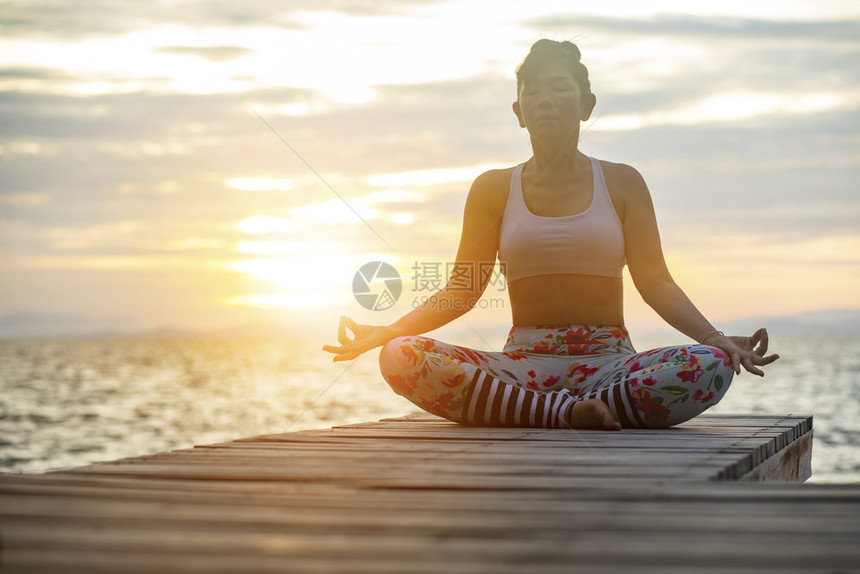 海滨打坐在瑜伽冥想中的女人在海边摆姿势对抗美丽的太阳升起天空年轻图片