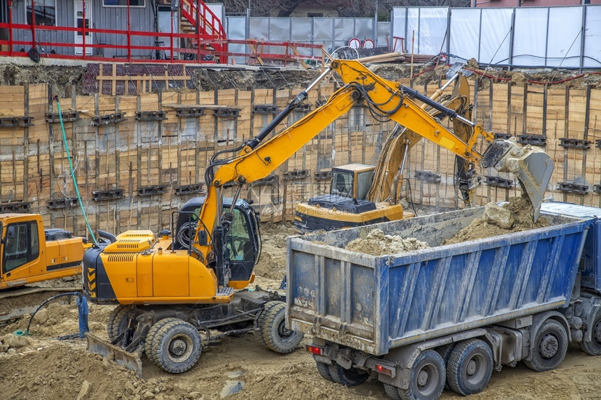 车辆挖掘机正在卡车上装载挖掘作业建筑工地的重型设备在施工中进行作铲地面图片