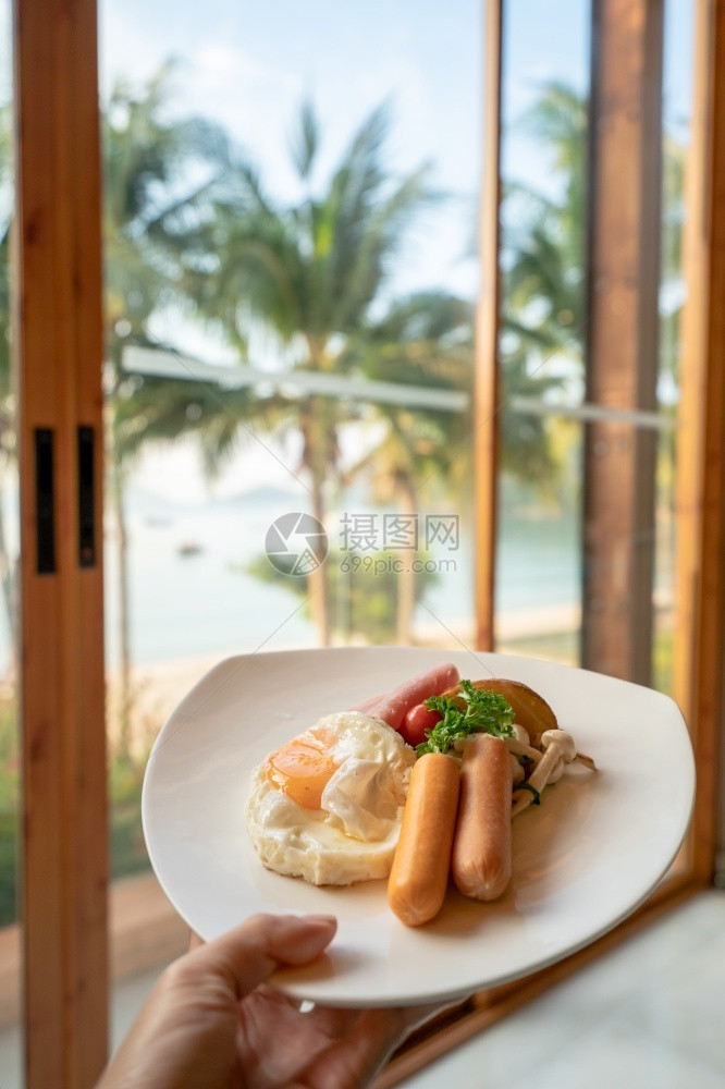 放开胃菜手拿着美国早餐上在海滩背景配有煎鸡蛋烤香肠和蔬菜沙拉的美式早餐食物图片