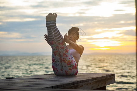 瑜伽士黎明女人在海边的木制码头上做瑜伽对抗美丽的太阳升起天空自然图片