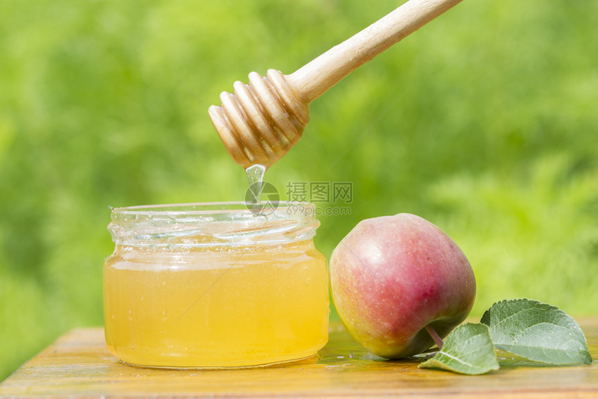 木制桌上的蜂蜜罐棍子和苹果新鲜的自然水图片