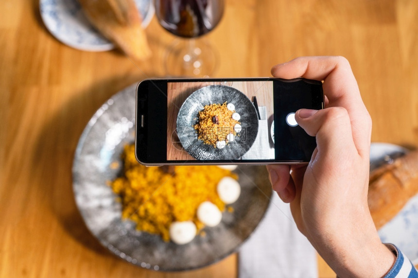 人类男子手持智能机在餐厅或咖啡馆拍摄食物高质量照片男子手持智能机在餐厅或咖啡馆拍摄食物保持喝图片