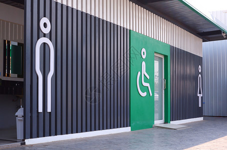泰国服务卫生间侧视图和关注男残疾人轮椅前景以及木板上女标志和公共厕所绿色墙装饰物上的女标志视角和重点背景图片