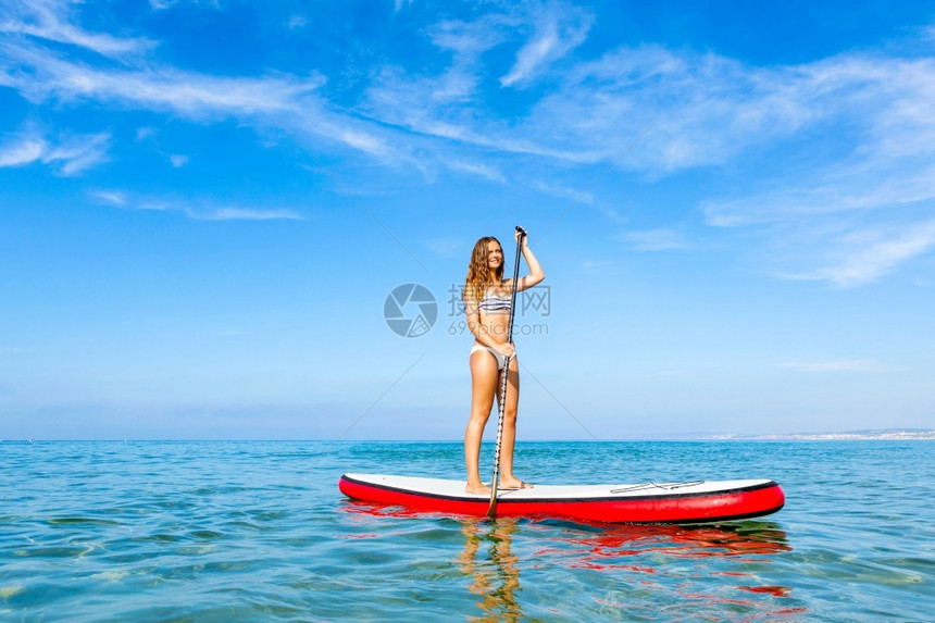 桨板冲浪一个美丽的女人在阳光明媚的日子里练习划桨青少年女士图片