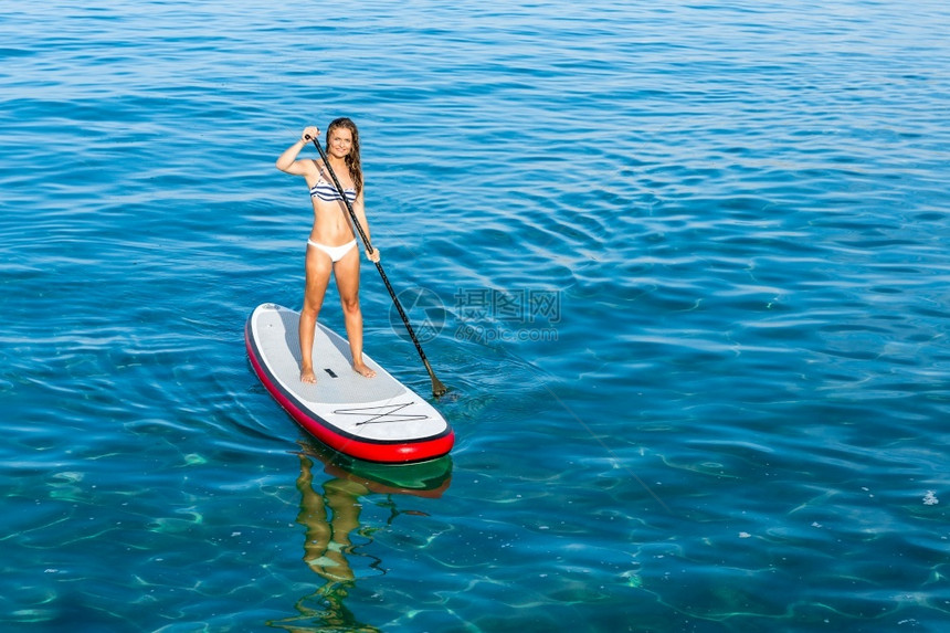 一个美丽的女人在阳光明媚的日子里练习划桨站立水锻炼图片