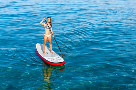 一个美丽的女人在阳光明媚的日子里练习划桨站立水锻炼背景图片