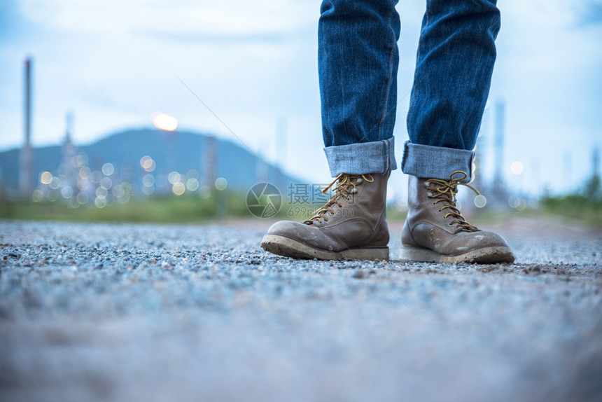 承包商步行在建筑工地的导管安全作人员程师穿着Jeans和BrownBoots在炼油工程师安全行业时装运动室外行走的背景上为工人提图片