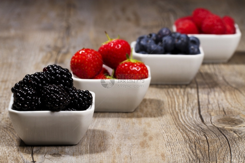 无刺莓小吃自然碗里有野生浆果一些碗里装满了野生浆果在前面的木本底黑莓上图片