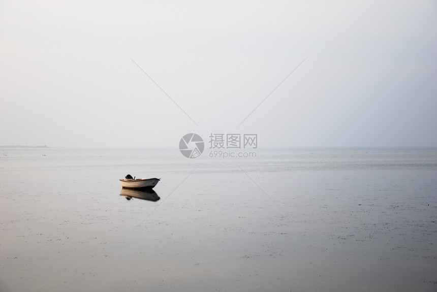 经过一种反射在条灰色和薄雾海岸的水中单独小划船图片