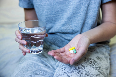 健康服用近距离坐在床上用水杯服药的穿睡衣女妇白种人图片