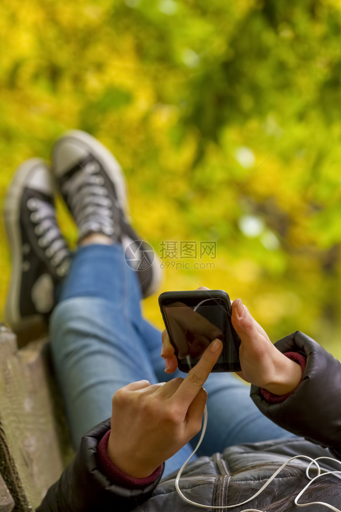 轻松城市女孩使用智能手机躺在秋天公园长椅上关注智能电话的青少年城市图片