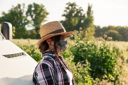 自然场地新冠戴草帽和外科面具靠在包车旁边的年轻农妇图片