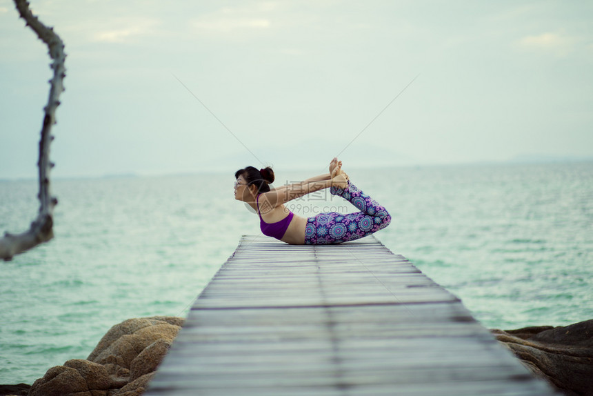 合身美丽的女人在海木码头做瑜伽在海龟上摆姿势漂亮的木制图片