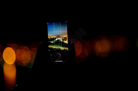 一个男人在智能手机上拍摄城市夜景照片图片