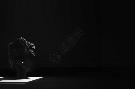 里面郁闷孤黑色和白的画面无望男人独自一坐在地上拥抱着他的膝盖在空暗房间里阳光和影子照在地板上背景图片