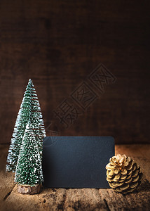 圣诞快乐新年在黑板上欢庆红木桌和黑色棕褐木墙壁贺卡上挂着Xmas树和金松果雪复制礼物图片