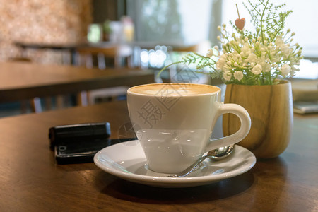 店铺咖啡桌上的杯在店装饰假花和手机上装饰假花饮料概念咖啡因泡沫图片