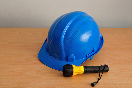 专业的握住黄色和蓝的塑料手电筒用蓝硬帽在木制背景上隔离力量图片