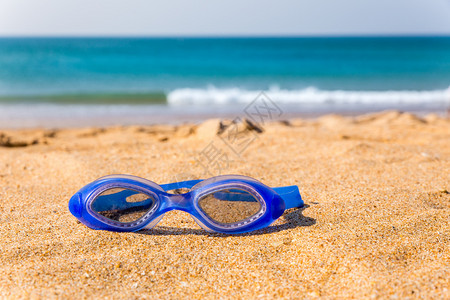 蓝色游泳护目镜躺在沙滩上背景图片