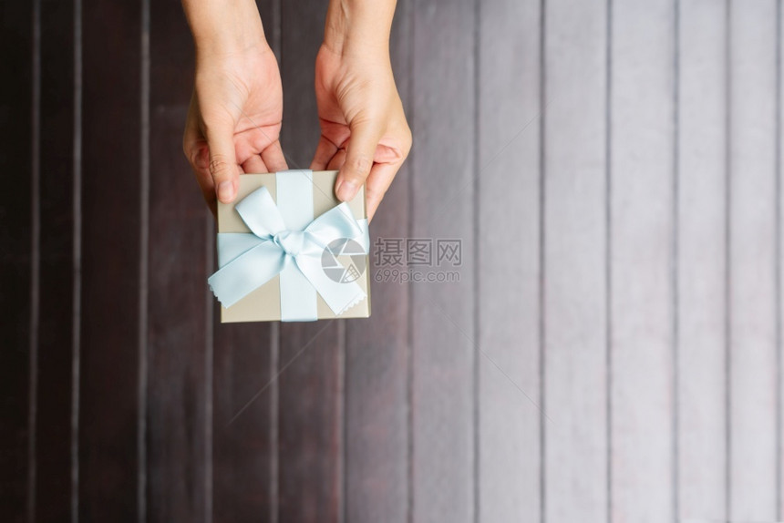 天手握小礼物包着蓝丝带装在木制背景上人们的图片